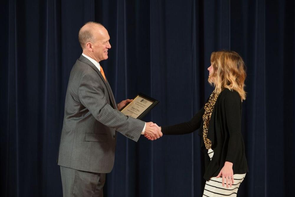 Doctor Potteiger shaking hands with an award recipient in a black sweater and a leopard print scarf